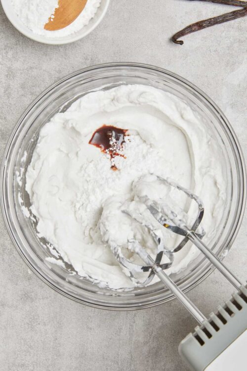 Fluffy whipped cream in a glass mixing bowl for baking recipes.