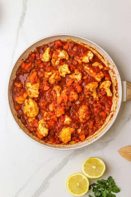 Savory cauliflower and carrot stew in a white skillet, garnished with fresh lemon and herbs for a healthy meal.