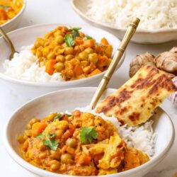 Savory chickpea curry with rice and naan bread on a white marble table.