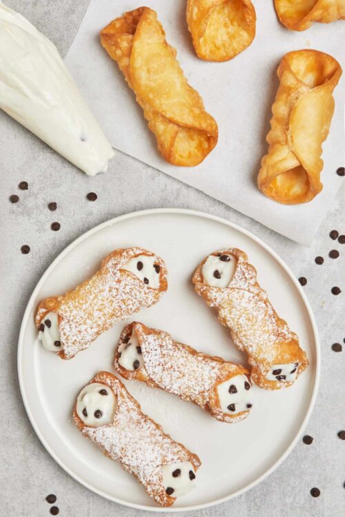 Fried dough snowmen cookies with white chocolate faces and chocolate chips, dusted with powdered sugar on a white plate.