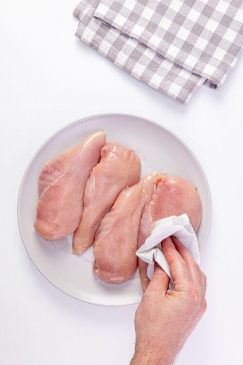 Raw chicken breasts on a white plate, ready for cooking or baking.