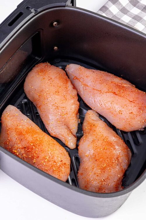 Juicy chicken breasts seasoned with spices in air fryer, ready to cook.