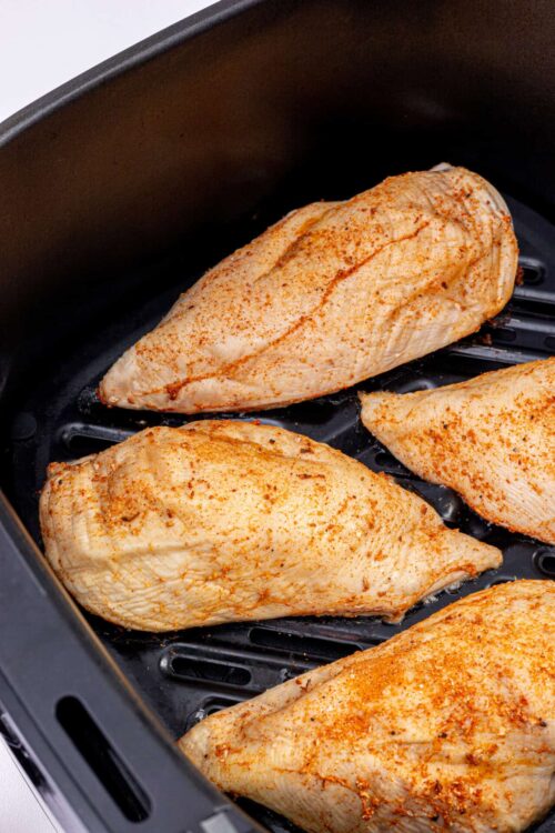 Seasoned chicken breasts in air fryer basket ready for cooking.