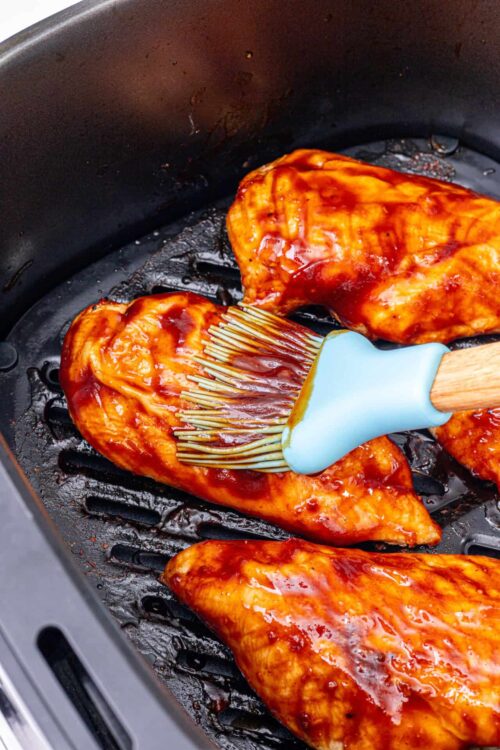 Juicy grilled barbecue chicken breasts being coated with sauce in a black grill pan.