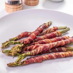 Bacon-wrapped grilled asparagus on a white plate with salt and pepper shakers in the background.