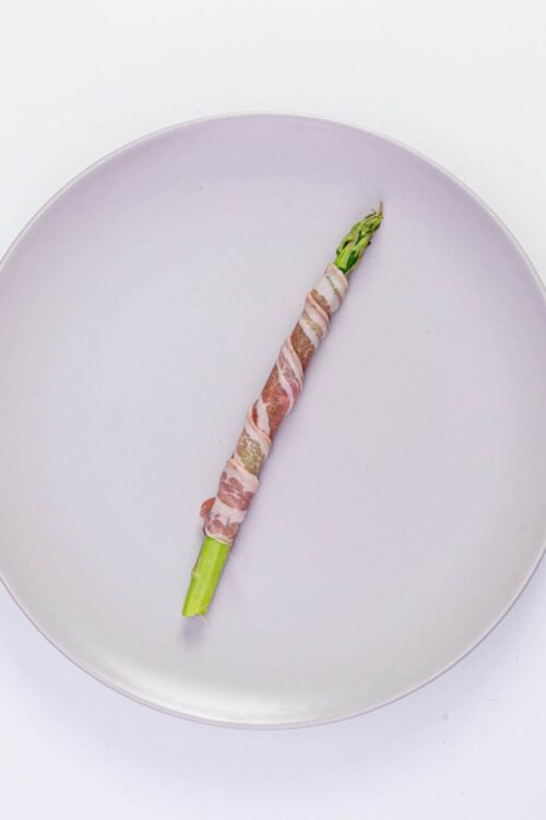 Bacon-wrapped asparagus on a white plate, healthy appetizer or snack option.
