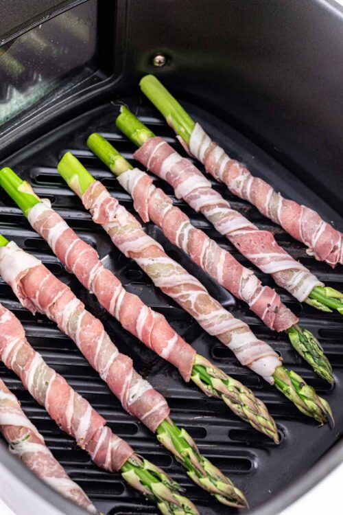 Bacon-wrapped asparagus spears in air fryer for a healthy appetizer or side dish.