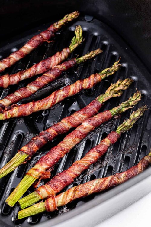 Bacon-wrapped asparagus spears cooking in air fryer for healthy snack or side dish.