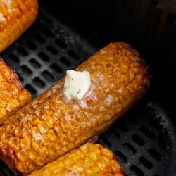 Golden roasted corn on the cob with butter in a black air fryer basket, crispy and seasoned perfectly.