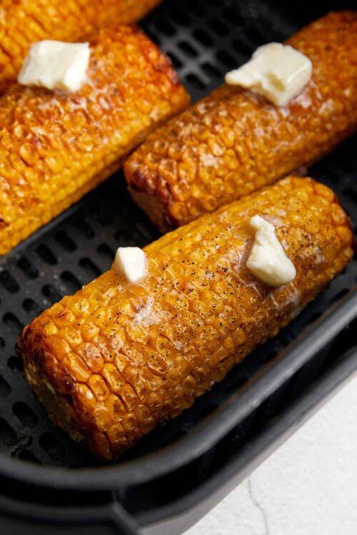 Corn on the cob with butter and seasoning on a black tray.