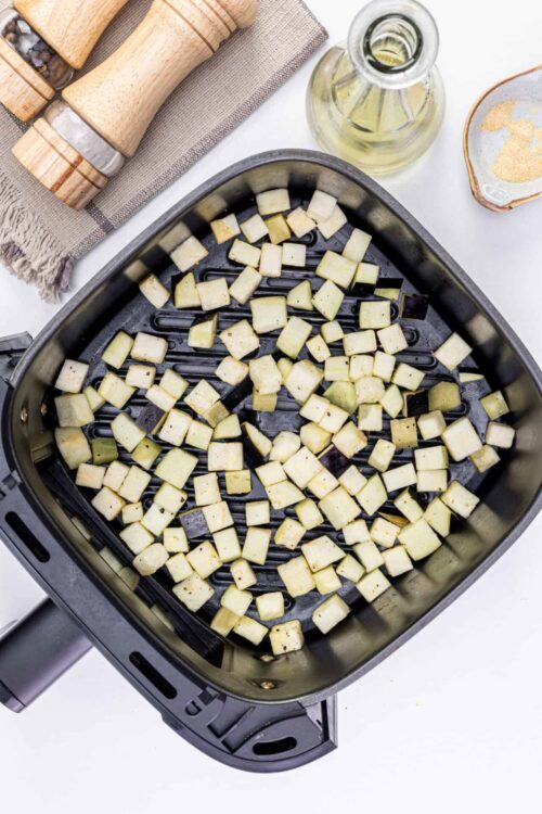 Roasted diced eggplant in air fryer on a white kitchen countertop with salt, oil, and seasoning.