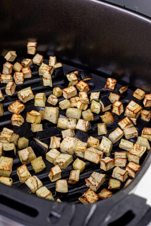 Roasted cubed eggplant in an air fryer basket.
