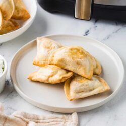 Golden baked empanadas on a white plate with a marble countertop and kitchen appliances in the background.