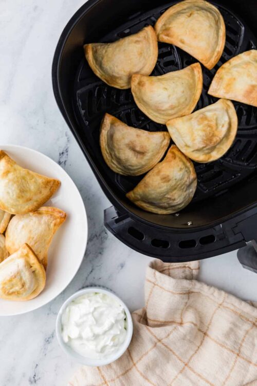 Flaky baked empanadas in air fryer with dipping sauce on side.