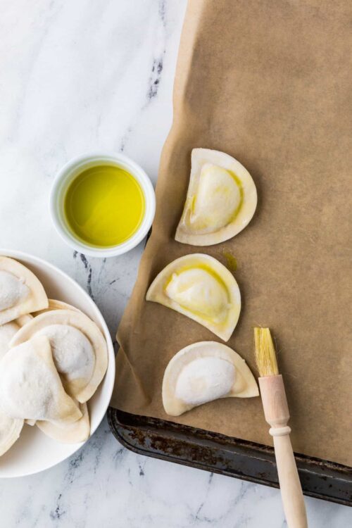 Golden cheese ravioli ready for cooking with olive oil and fresh pasta on baking sheet.