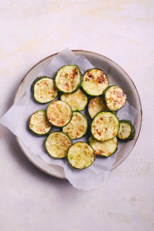 Roasted zucchini slices with melted cheese on a white ceramic plate.