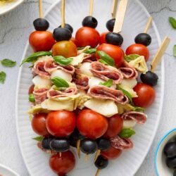 Colorful appetizer platter with cherry tomato, mozzarella, prosciutto, and basil skewers.