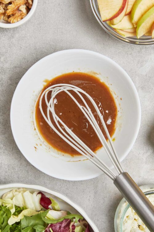 Creamy tomato soup with a whisk, garnished with swirls of cream in a white bowl.