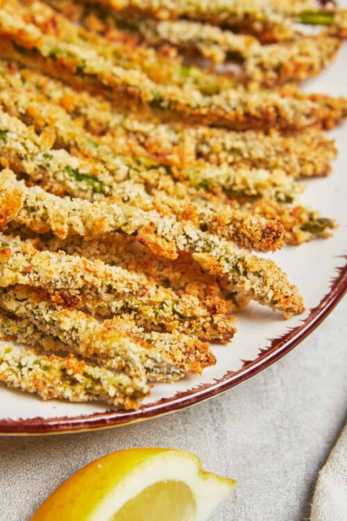 Crispy lemon herb baked fish fillets on a platter with lemon wedge for a healthy seafood recipe.