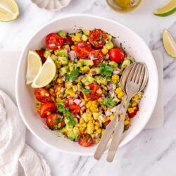 Fresh tomato cucumber corn salad with lime and cilantro on white bowl.