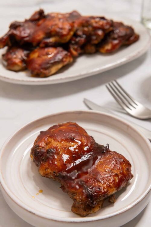 Juicy glazed BBQ chicken leg on a white plate with a crispy caramelized exterior.