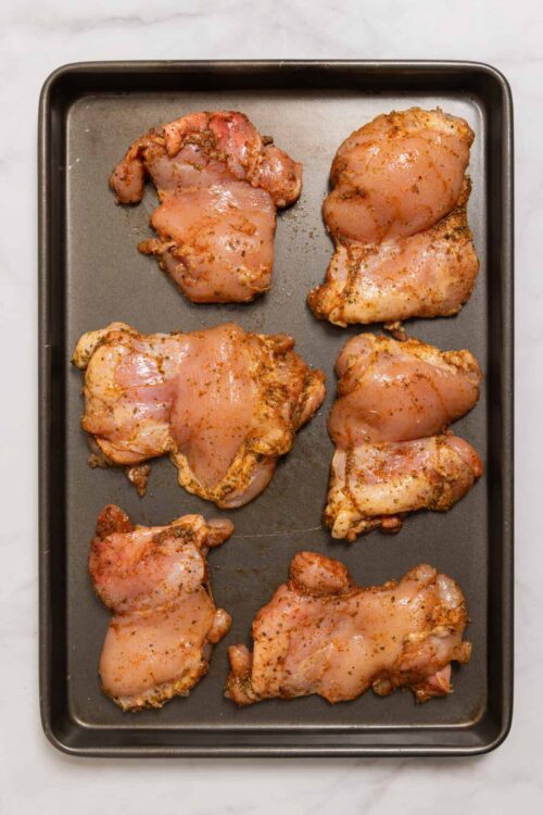 Raw seasoned chicken thighs on a baking sheet for roasting.