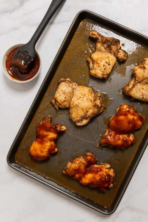 Juicy baked chicken thighs with barbecue sauce on a baking sheet. Perfect for weeknight dinners and family meals.
