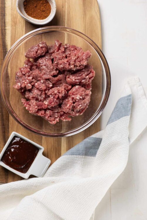 Ground beef for meatloaf with spices and sauces, on a wooden cutting board.