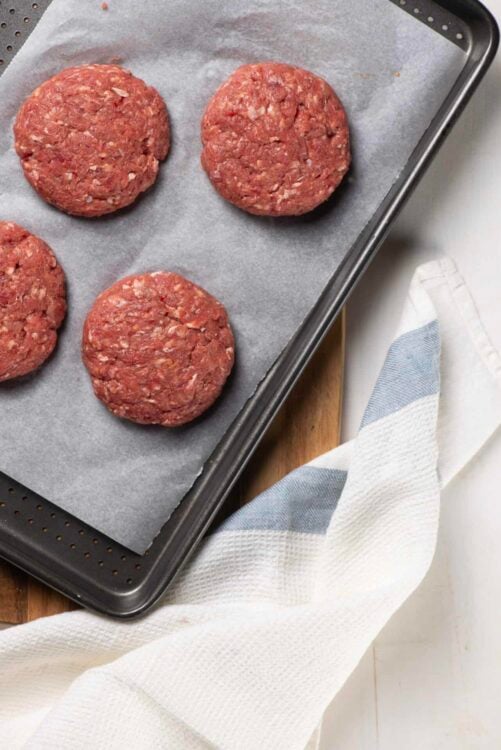 Seasoned ground beef patties on parchment paper before grilling or baking.