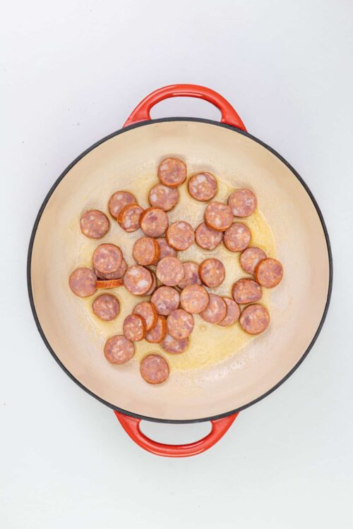 Crispy sausage slices in cast iron skillet on white background.