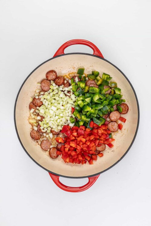 Sautéed sausage with chopped onions, green bell peppers, and red bell peppers in a skillet.