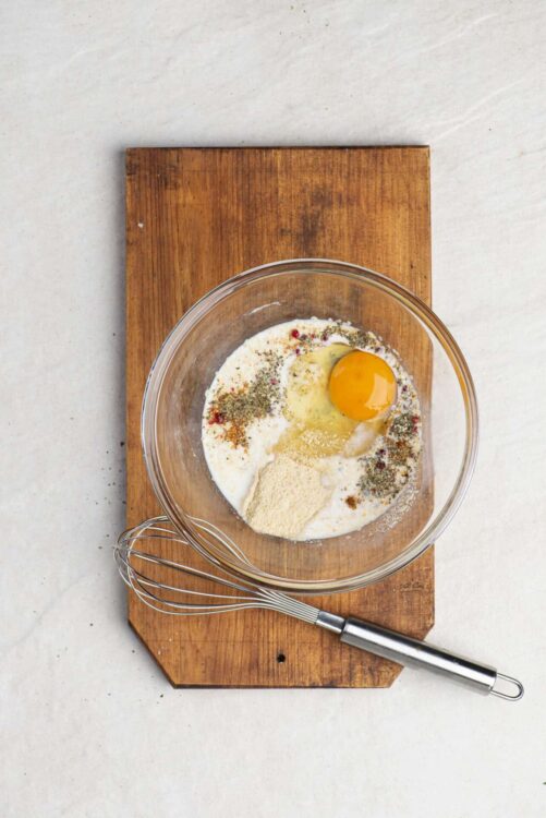 Cream mixture with eggs and spices in glass bowl on wooden cutting board, ready for baking.
