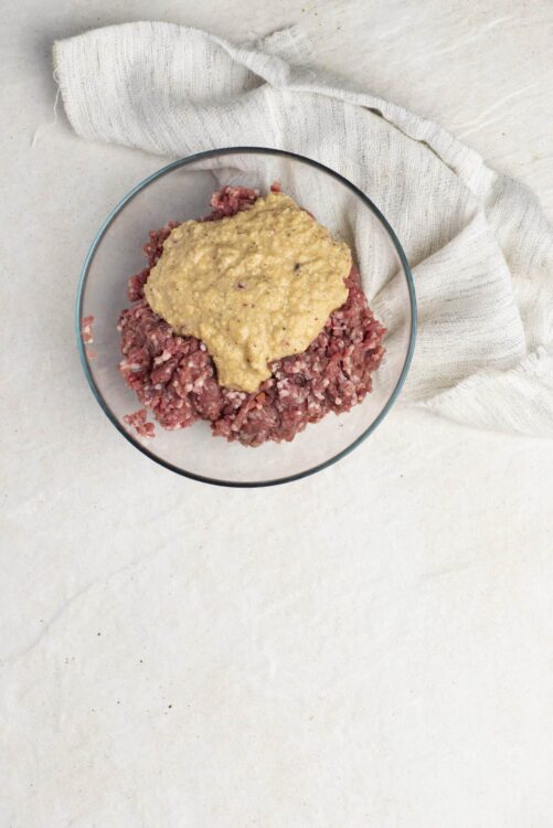 Seasoned ground beef with minced garlic and herbs in a glass bowl.