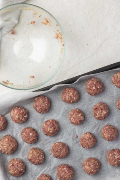 Golden raw meatball mixture on baking sheet with parchment paper, ready to bake.