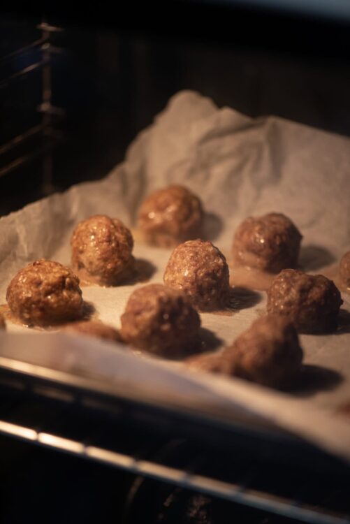 Golden baked meatballs cooling on parchment paper in an oven.