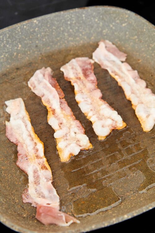 Crispy bacon strips sizzling in a non-stick skillet.