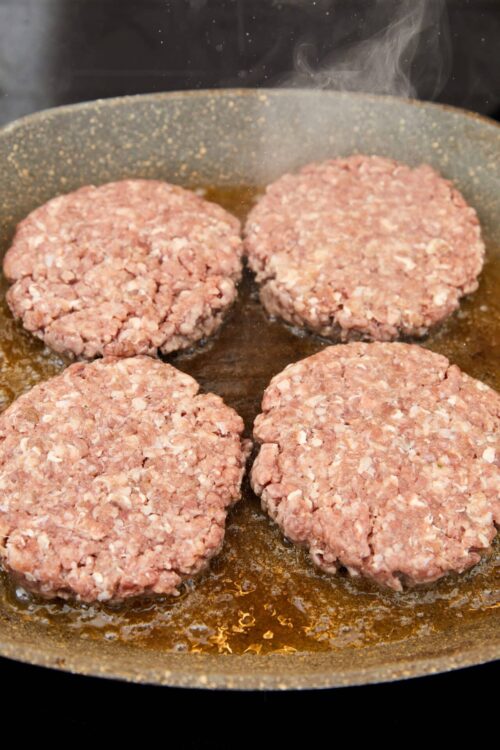 Savory burger patties cooking in a skillet, sizzling and browning, mouthwatering homemade burgers, lunch or dinner idea, Baked Bree recipe.