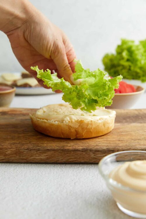 Fresh lettuce being added to a sandwich bun with mayonnaise.