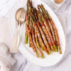 Bacon-wrapped grilled asparagus spears on serving platter with salt and pepper shakers.