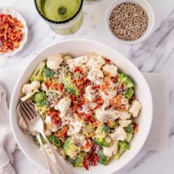 Golden sunflower seed snack and vegetable salad with broccoli, cauliflower, and bacon on a white plate.