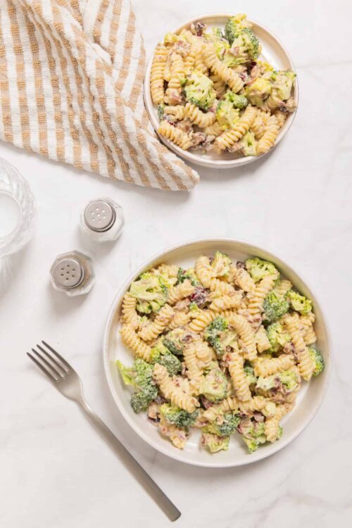 Creamy broccoli bacon pasta salad with rotini and fresh vegetables, served on a white plate.