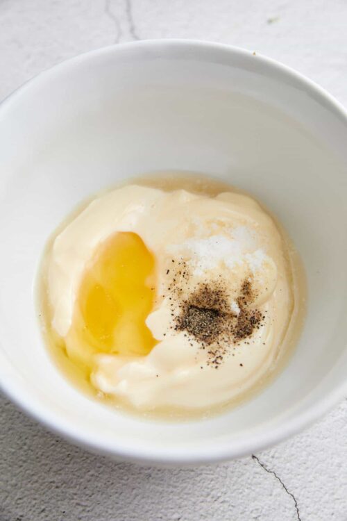Creamy mixture of eggs, mayonnaise, and spices in a white bowl for baking or cooking recipes.