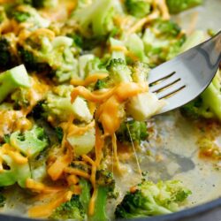 Steamed broccoli with melted cheese in a skillet, close-up of cheesy broccoli dish.