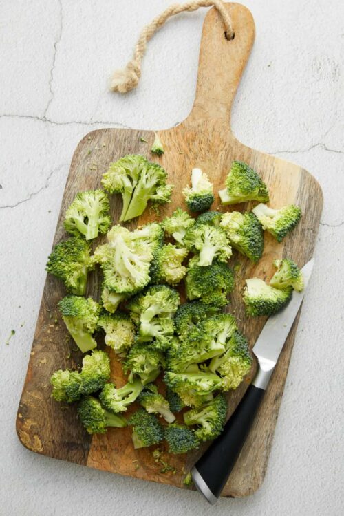 Fresh broccoli florets on wooden cutting board for healthy cooking or prep.