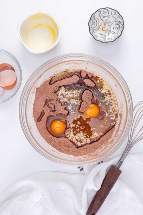 Cream, eggs, cocoa powder, and flavorings in a mixing bowl for baking recipe.