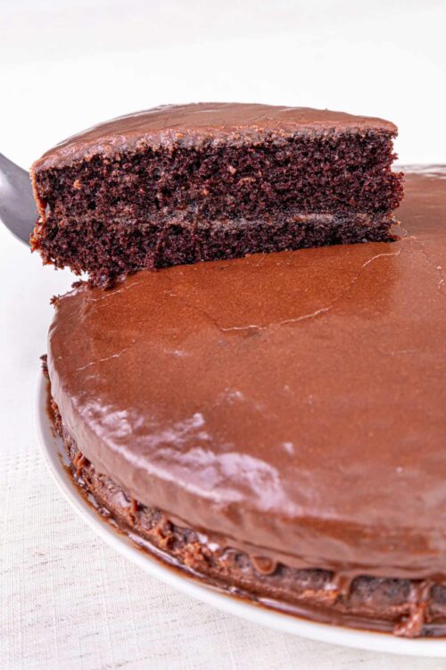 Decadent chocolate cake with glossy chocolate ganache and a slice lifted.