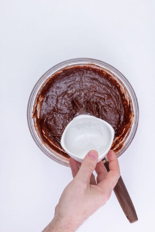 Rich chocolate cake batter being mixed with milk in a glass bowl for baking.
