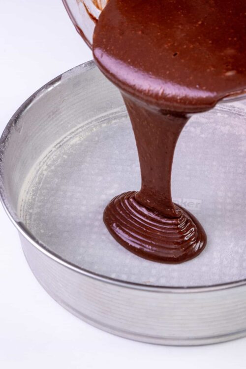 Rich chocolate ganache being poured into a cake pan.
