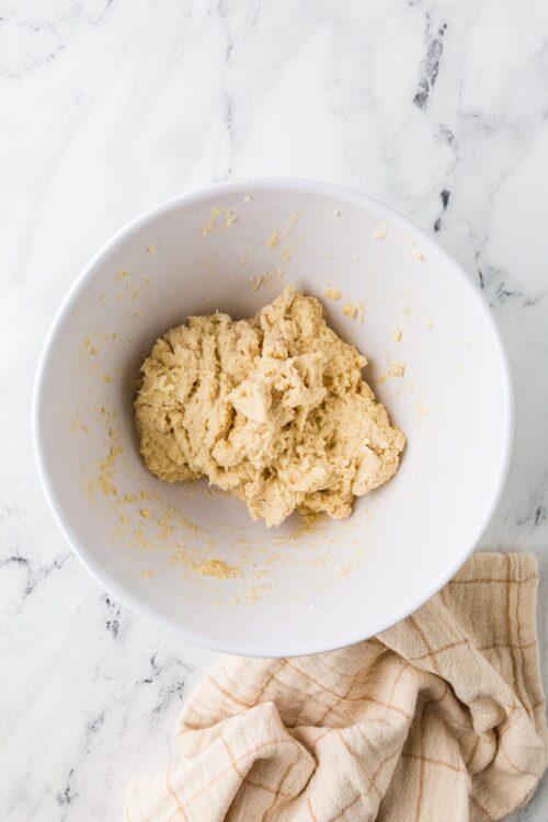Butter cookie dough in a white bowl on marble surface with beige cloth.