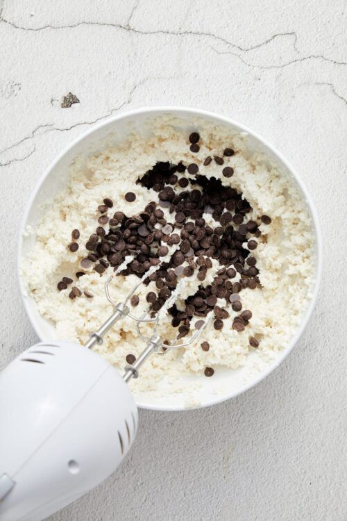 Cream cheese frosting with chocolate chips in a mixing bowl.